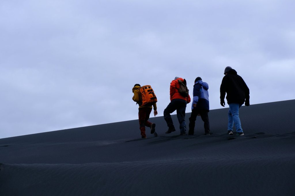 People are hiking up a sand dune.